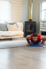 Man performing push-ups on blue exercise mat on wood floor in living room near wood-burning stove