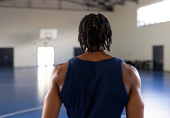 African American man wearing navy tank top standing facing wall-mounted hoop on blue court in gym
