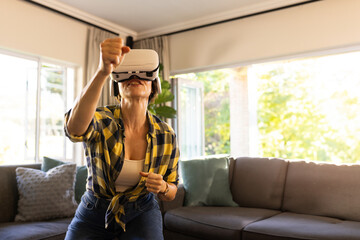 Woman standing in living room wearing VR headset and throwing punch toward grey sofa with pillows