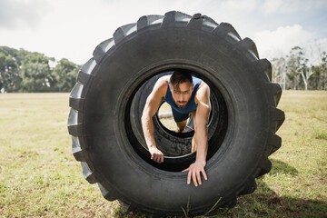 Male athlete crawling through large tractor tire on grassy field with obstacle course