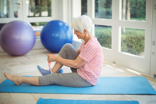 Senior woman stretching on blue exercise mat in home gym with stability balls, copy space