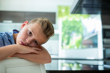 Male child resting head on chair back in kitchen with stainless-steel hood, copy space
