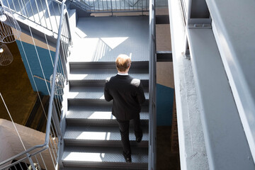 Metal staircase rising in industrial stairwell, sunlight casting geometric shadows on steel steps