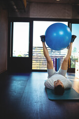 Man wearing workout clothes lifting blue stability ball with legs on exercise mat in fitness room