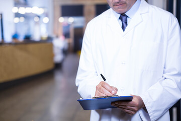 Medical doctor writing on blue clipboard with pen in reception corridor wood panel desk