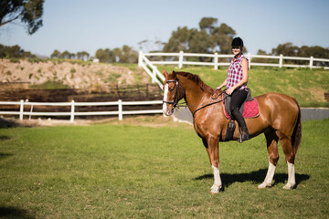 Female equestrian wearing helmet riding chestnut horse with red saddle pad in paddock, copy space © wavebreak3