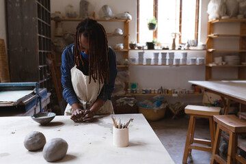 African American woman kneading clay at ceramics workshop table wearing apron with pottery tools