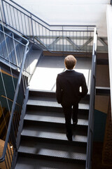 Business male ascending steel staircase with handrails in industrial stairwell lighting white walls