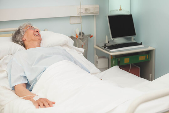 Senior woman resting on hospital bed with IV line and monitor on bedside table, copy space - Powered by Adobe