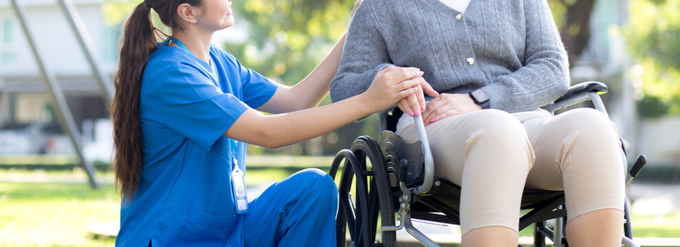 Young caucasian nurse comforting with patient while sitting on wheelchair in outdoor park, doctor woman support and counseling with patient, caregiver and service, medical and consoling.
