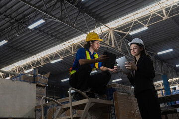 Industrial warehouse workers wearing safety helmets using digital tablets to discuss inventory control and logistics operations inside a modern factory or distribution center.