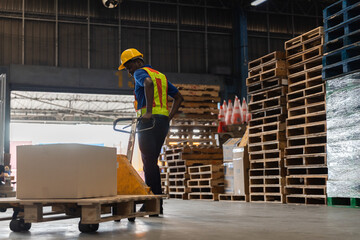 Warehouse worker in safety gear using a pallet jack to move cardboard boxes inside a distribution center. Industrial logistics concept showing manual handling in supply chain operations.