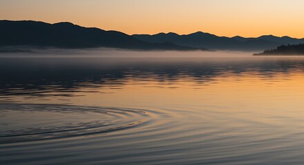 Obraz premium Lake at Sunrise with Ripples and Misty Mountains