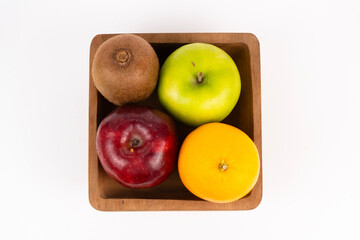 A square wooden bowl holds four colorful pieces of whole, fresh fruit.