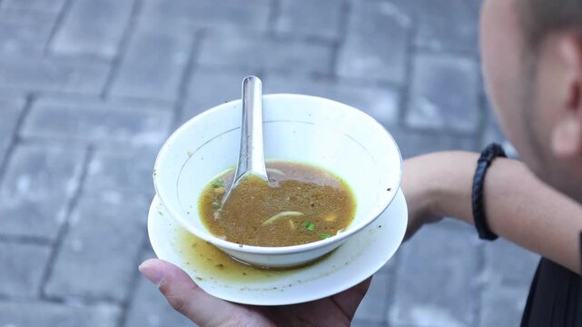rear view, a man is eating chicken soto which is almost finished in a white bowl.
