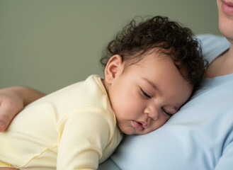 curly haired baby sleeping peacefully on adult's chest in gentle embrace, close up showing tender bonding and comfort