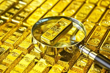 Gold bar on magnifying glass for Imitation gold, fake ,faux or real gold concept. Gold is hard commodity goods, risk asset, tangible value, save assets during war and economic crisis