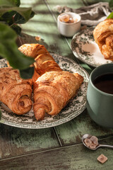 Breakfast on wooden table with croissants, coffee and apples in bright light of the morning sun. Cozy rustic autumn food concept