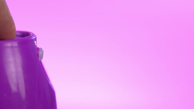 Extreme close up of a finger pressing spray nozzle, releasing product against blue and purple gradient background.