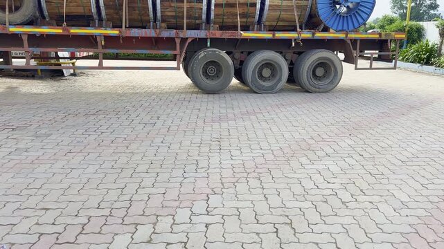 Tilt-up shot of a flatbed truck loaded with large industrial wooden cable drums secured with straps, parked in a paved yard.