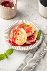 Cottage cheese pancakes or syrniki with raspberry jam on ceramic plate on light gray kitchen table. Healthy sweet breakfast