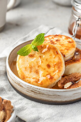 Cottage cheese pancakes or syrniki with walnuts and honey on ceramic plate on light gray kitchen table close up. Healthy sweet breakfast