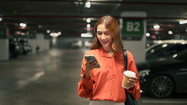 Smiling young woman checking smartphone while holding coffee cup in an underground parking lot