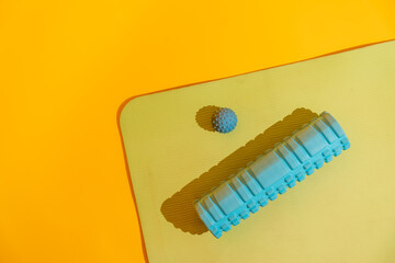 Top view corner of yoga mat with massage ball and foam roller casting long shadows on yellow bright studio. High quality photo