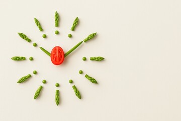 A intermittent fasting clock face made with asparagus, green peas, and a tomato, healthy eating and the passage of time.