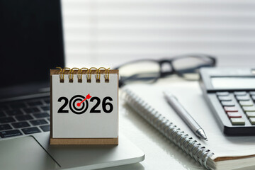 Desk calendar showing 2026 with a target icon on an office workspace beside calculator, notebook, pen and laptop, symbolizing financial planning, budgeting, goals and KPI strategy for the new year.