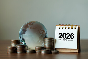 Stacked coins beside a glass globe and a desk calendar marked 2026 illustrate financial planning, investment strategy, savings growth, and global economic goals for the new year with ample copy space.