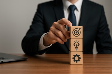 Hand arranging wooden business blocks with goal, lightbulb, and gear icons on table
