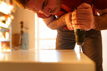 Carpenter using drill while assembling furniture in woodshop