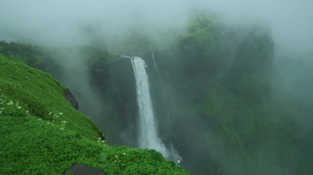 Slow motion shot of Kalu waterfall during the severe rainy storm with clouds surrounding it as seen from a nearby cliff at Malshej Ghat region of Maharashtra, India. Scenic view of strong waterfall.