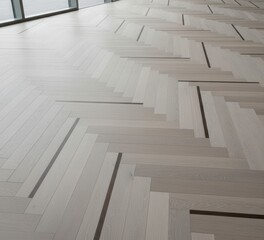 Obraz premium Modern parquet flooring with a herringbone pattern in light wood and grey tones. An elegant background for interior design, home renovation, or real estate.