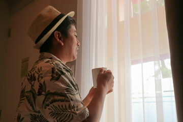 silhouette of young asian man drinking coffee in window with view of blue sea in luxury beach resort of bali. Sunrise on vacation.