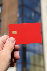 Hand holding blank red chip credit card outdoors