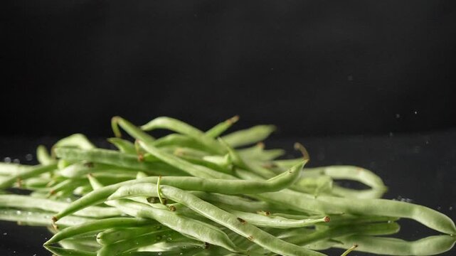 Slow motion shot of fresh beans falling and bouncing towards camera on black background. Premium legume footage perfect for health food commercials and cooking content.