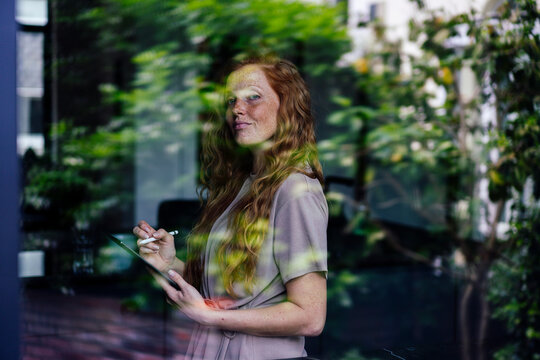 Smiling freelancer with tablet PC seen through glass window