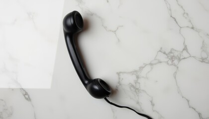 Black telephone receiver on marble surface with cord  