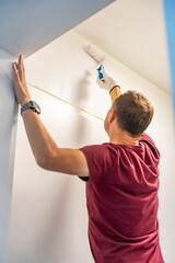 Man painting the wall with a roller in white during home renovation. Interior improvement, surface transformation and DIY work with paint tools.