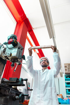 Lab technician in protective helmet and coat working with industrial drill