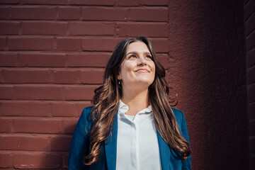 Confident businesswoman in blazer standing outdoors by brick wall
