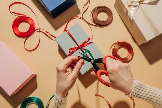 Hands wrapping Christmas gift with ribbon on festive table