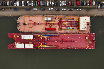 Brooklyn, United States - 29 August 2021: Aerial view of two large ships with red and pink decks contrasting against the dark water, docked beside a row of parked cars.