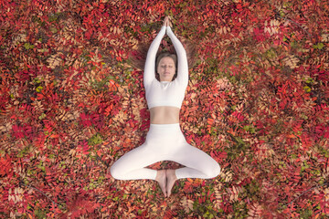 Woman practicing yoga in a peaceful autumn setting surrounded by colorful leaves while focusing on her health and mindfulness. A woman practices yoga on autumn leaves, top view flat lay