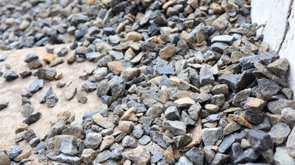Pile of gravel sits beside a concrete wall, creating a textured surface with varying shades of gray...