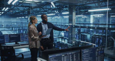 Working Together in a High-Tech Data Center, Black Male IT Specialist and Female Cybersecurity Expert Review Security Logs on a Laptop, Strengthening the Network's Defenses Against Potential Threats