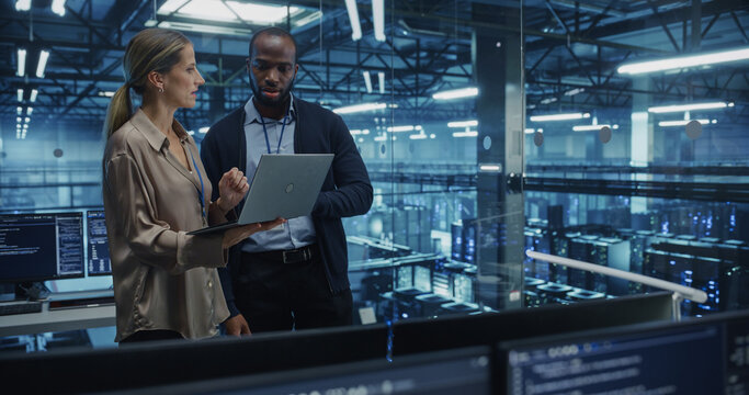 Male Cloud Architect and Female Database Engineer Review Data Storage Protocols on a Shared Laptop in a Data Center. Team Strategizing Ways to Improve Service for Enterprise Clients - Powered by Adobe