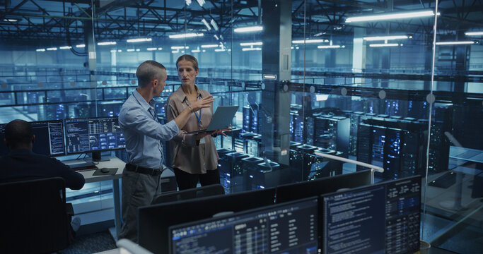 Diverse Team of Engineers Collaborating in a High-tech Data Center, Analyzing Server Performance on a Laptop Computer. Specialists Reviewing System Logs to Ensure Minimal Downtime Across the Network